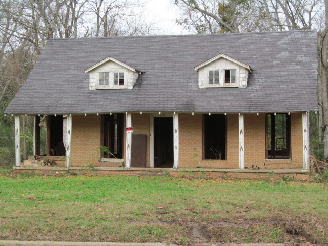 Front porch is visible, minus the overgrown trees